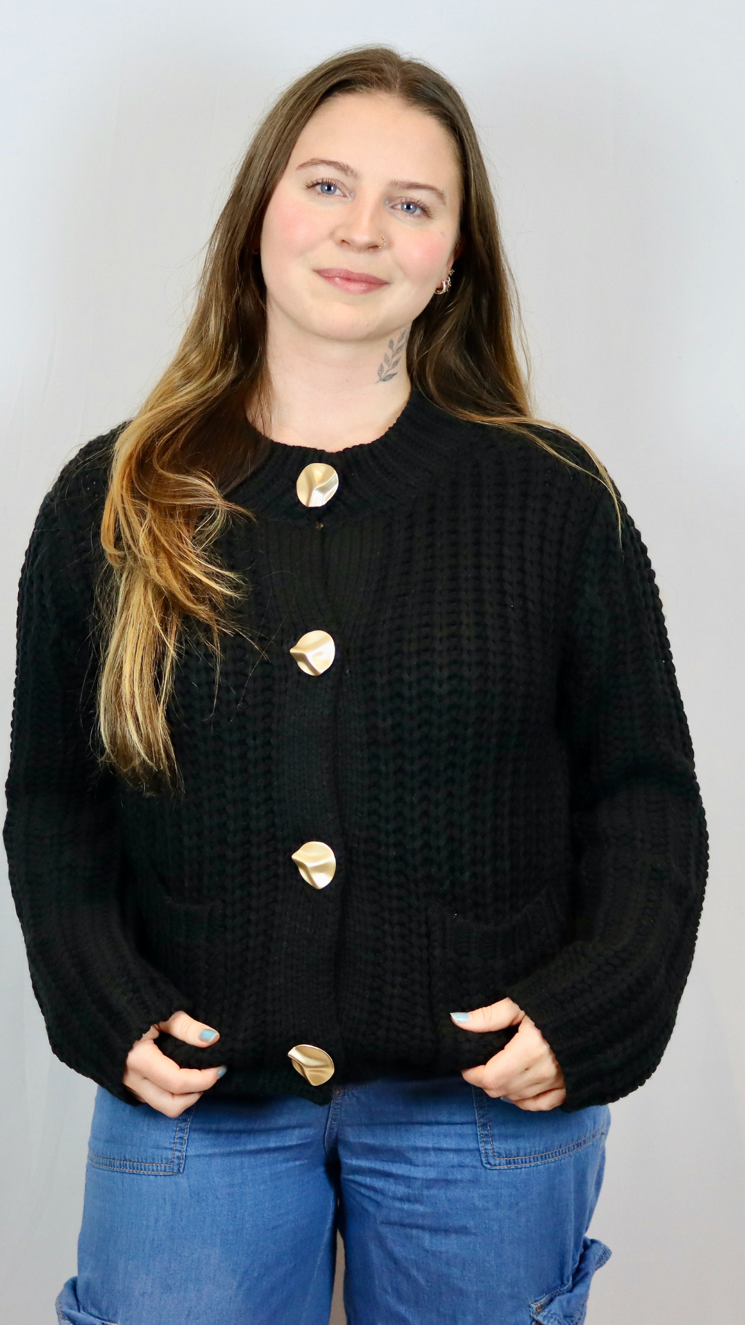 Chunky black ribbed knit cardigan with sculptural gold buttons and front patch pockets.